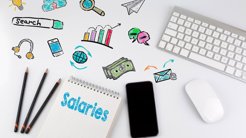 Computer keyboard, smartphone, pencils, and notepad that says "Salaries" next to internet-related icons.