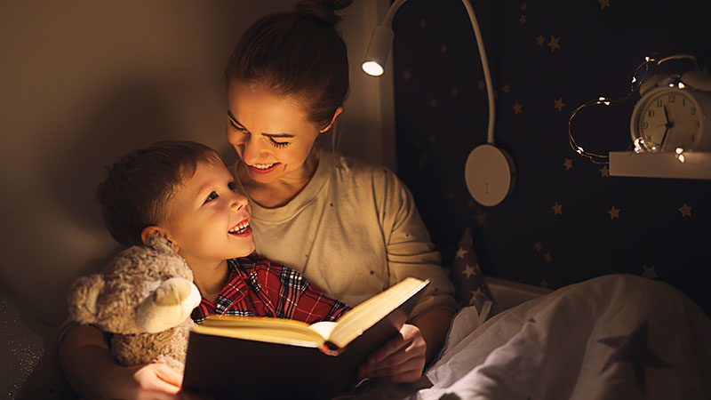 Mother and young son reading a book together in bed.