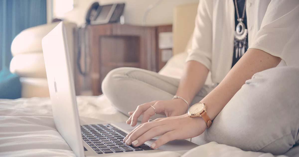 Woman sitting on bed typing in laptop.