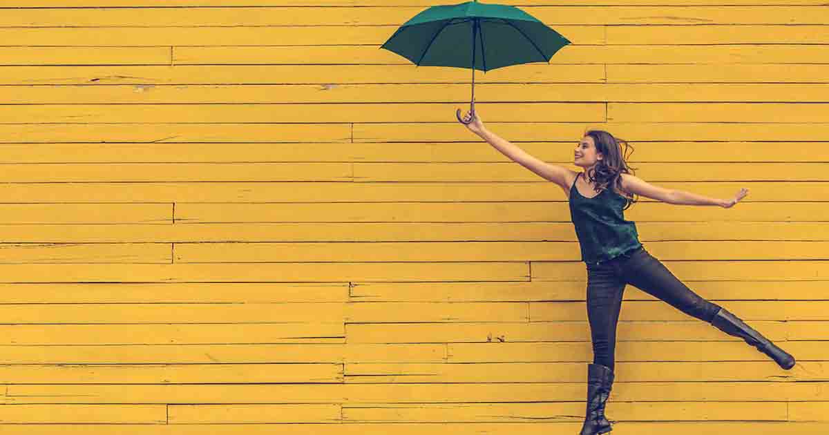 Smiling woman holding umbrella in front of yellow wall.